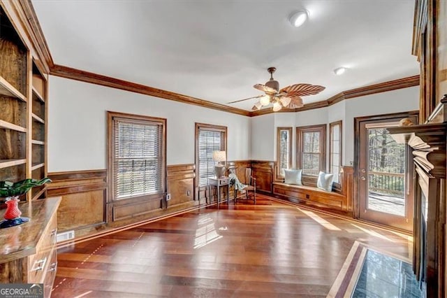 unfurnished room with a wainscoted wall, wood finished floors, a ceiling fan, and crown molding