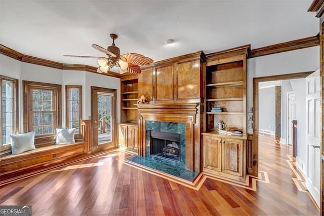 unfurnished living room with crown molding, built in shelves, wood finished floors, and a high end fireplace