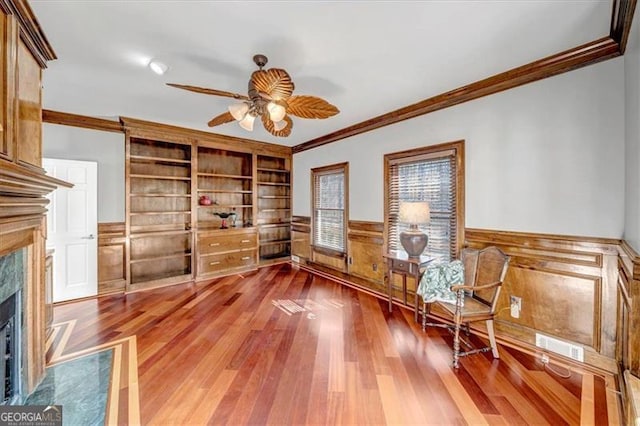 sitting room with a premium fireplace, crown molding, wood finished floors, and wainscoting