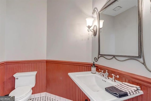 half bath featuring a sink, a wainscoted wall, and toilet