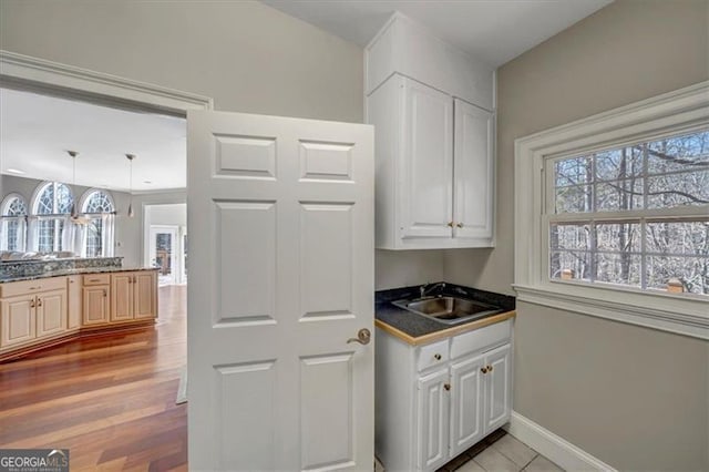 kitchen with light wood-type flooring, a sink, dark countertops, white cabinets, and baseboards