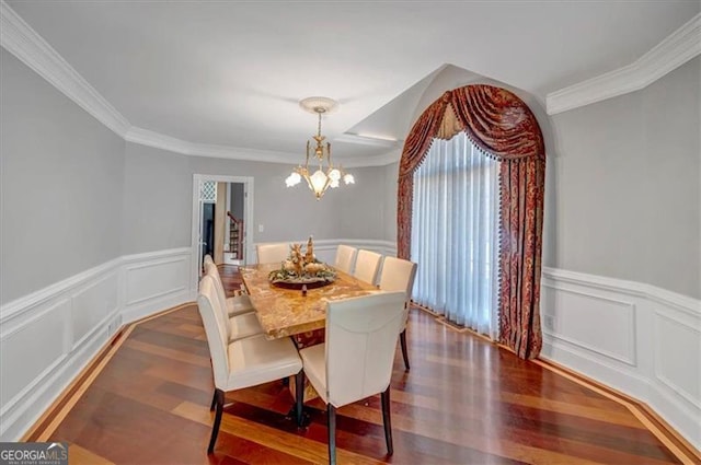 dining space with dark wood finished floors, crown molding, a notable chandelier, and a wainscoted wall