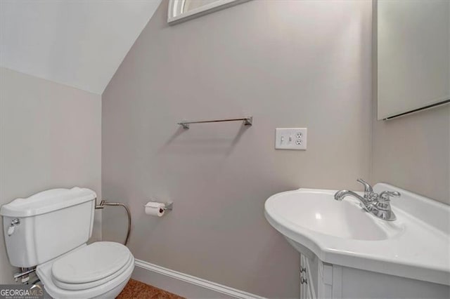 bathroom featuring baseboards, toilet, lofted ceiling, and a sink