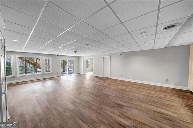 unfurnished living room featuring visible vents, a drop ceiling, baseboards, and wood finished floors