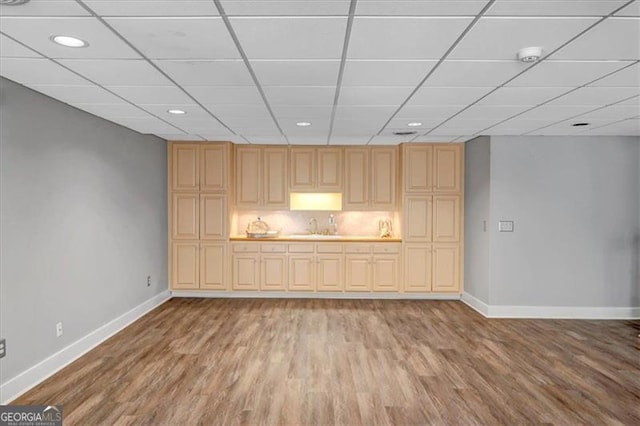 interior space featuring light wood-style flooring, a paneled ceiling, baseboards, and a sink