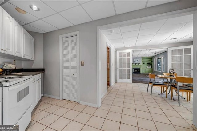 kitchen featuring light tile patterned floors, a fireplace, a drop ceiling, white cabinets, and white stove