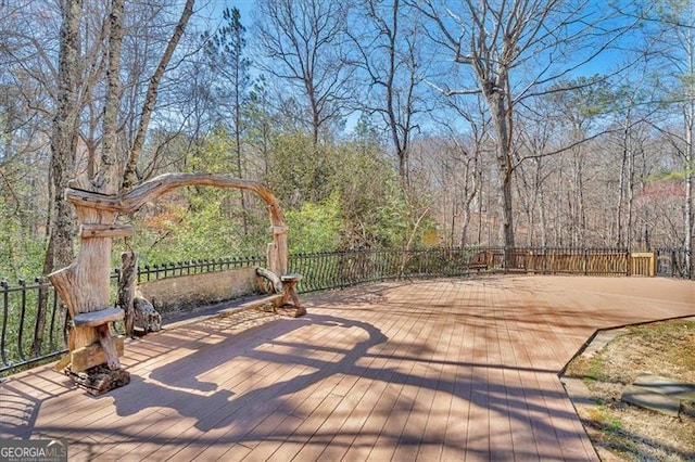 wooden terrace featuring a wooded view and fence