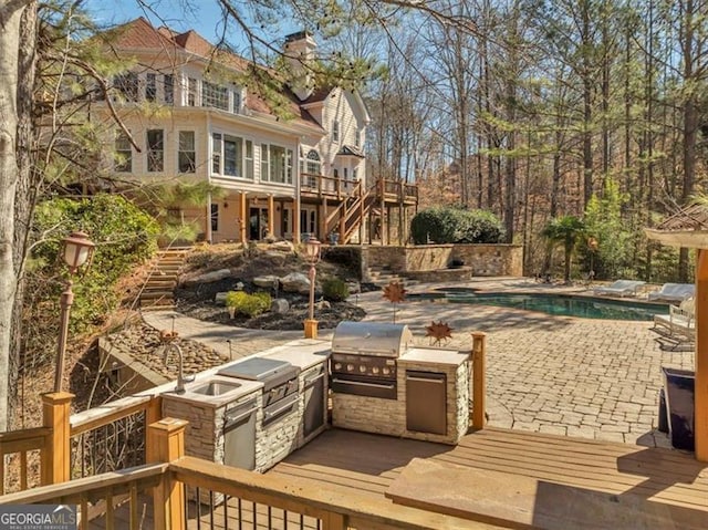 exterior space featuring a wooden deck, exterior kitchen, stairs, area for grilling, and an outdoor pool