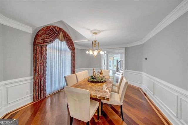 dining space featuring a notable chandelier, dark wood-type flooring, ornamental molding, and a decorative wall