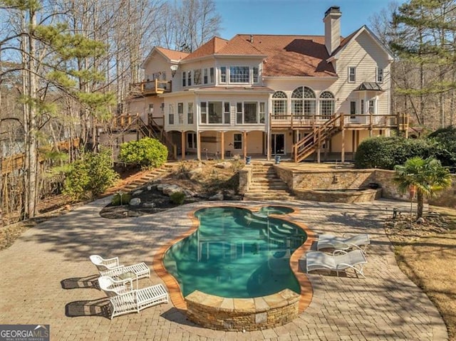 back of property with a wooden deck, a pool with connected hot tub, a chimney, stairs, and a patio area