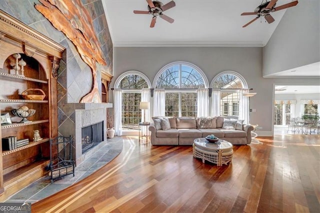 living room with a tiled fireplace, ornamental molding, built in shelves, and hardwood / wood-style flooring