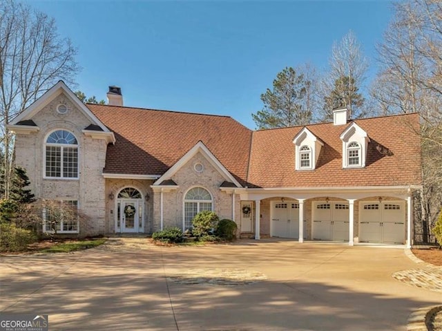 view of front of home with concrete driveway, an attached garage, brick siding, and a chimney