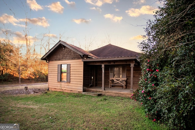 rear view of property featuring a shingled roof, a porch, and a yard