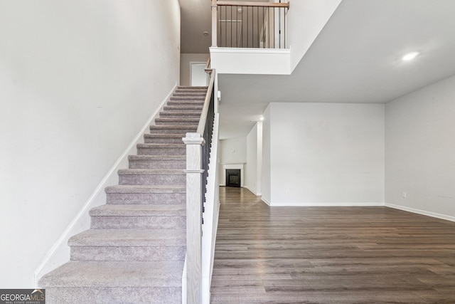 stairway featuring a fireplace, baseboards, wood finished floors, and recessed lighting