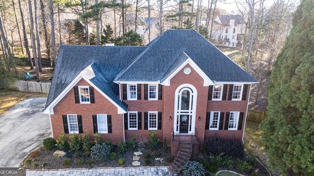 colonial house featuring roof with shingles, fence, and brick siding