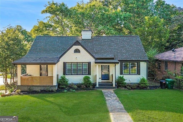 view of front facade featuring brick siding, a chimney, a front yard, and a shingled roof