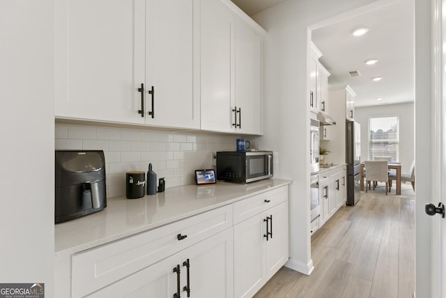 bar with tasteful backsplash, visible vents, light wood-style flooring, appliances with stainless steel finishes, and recessed lighting