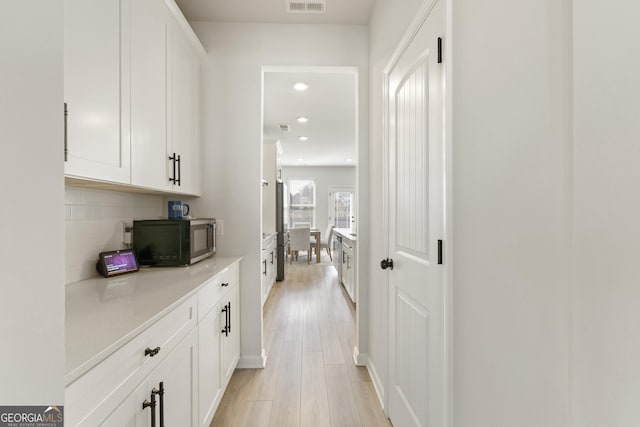 hall featuring light wood finished floors, visible vents, and recessed lighting