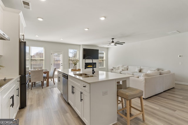 kitchen with a breakfast bar, visible vents, stainless steel dishwasher, freestanding refrigerator, and a sink