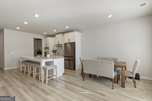 kitchen with a center island with sink, visible vents, freestanding refrigerator, white cabinets, and light wood-type flooring