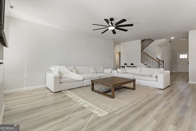 living room featuring baseboards, visible vents, a ceiling fan, stairway, and light wood-type flooring