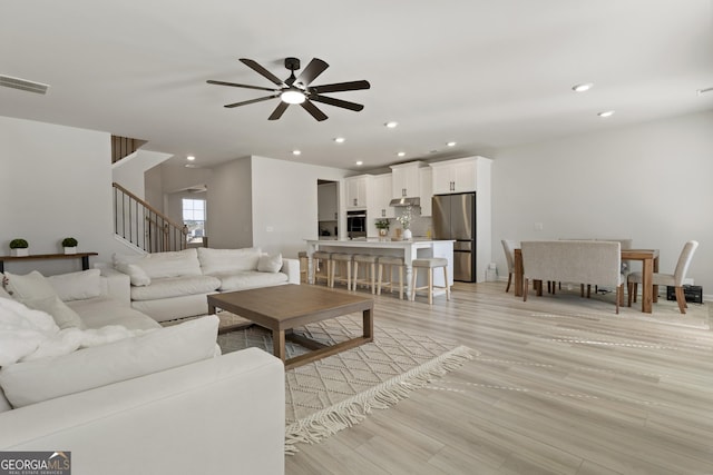 living room featuring visible vents, a ceiling fan, stairway, light wood-style floors, and recessed lighting