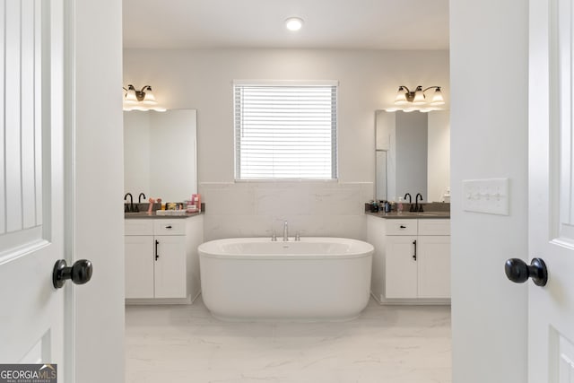 bathroom featuring marble finish floor, two vanities, a freestanding tub, and a sink