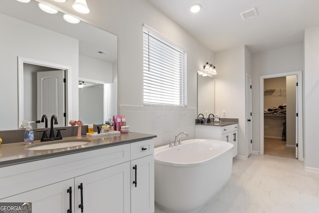 bathroom with a freestanding tub, marble finish floor, visible vents, and a sink