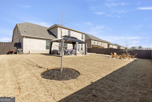 rear view of house with a fenced backyard, a fire pit, brick siding, a gazebo, and a patio area