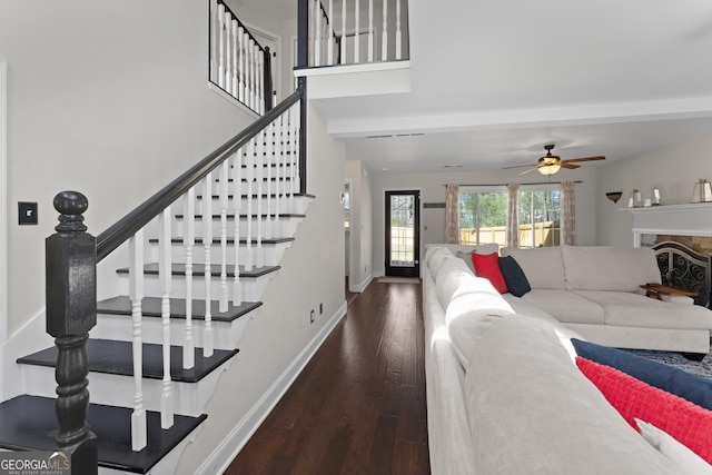 living area featuring baseboards, a ceiling fan, stairway, wood finished floors, and a stone fireplace