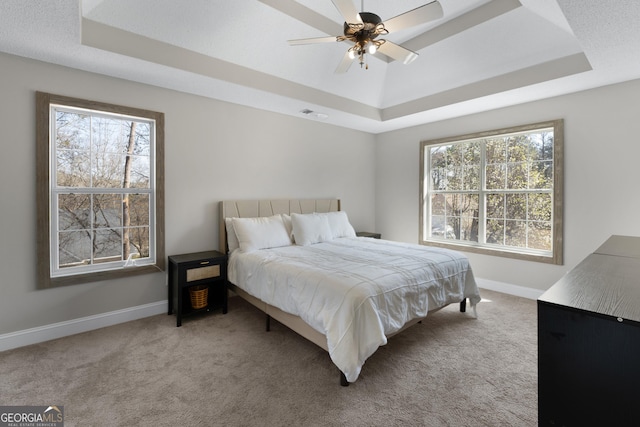 carpeted bedroom with a tray ceiling, multiple windows, and baseboards