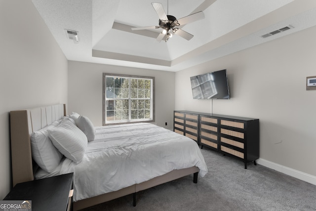 carpeted bedroom with a ceiling fan, a raised ceiling, visible vents, and baseboards