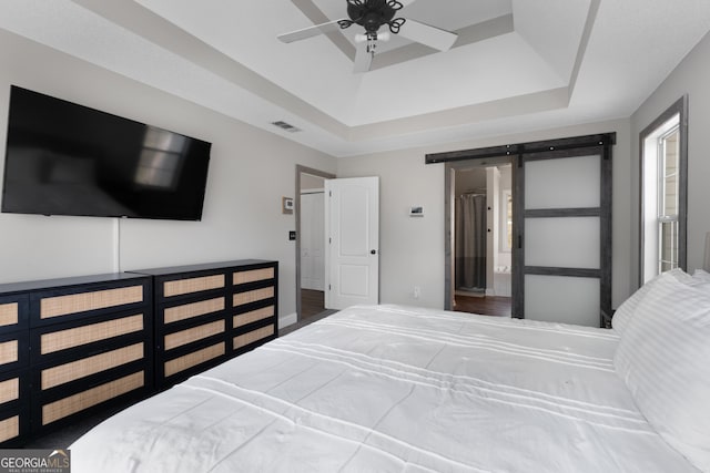 bedroom featuring a ceiling fan, a barn door, visible vents, and a tray ceiling