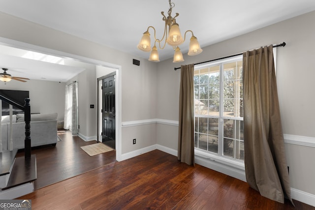 unfurnished dining area featuring ceiling fan with notable chandelier, hardwood / wood-style floors, and baseboards