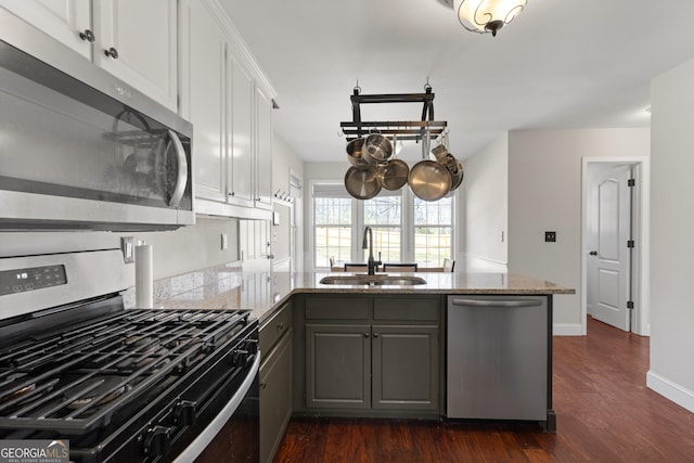 kitchen with stainless steel appliances, gray cabinetry, dark wood-type flooring, a sink, and a peninsula