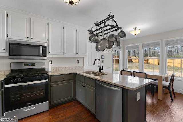 kitchen with appliances with stainless steel finishes, dark wood-style flooring, a peninsula, white cabinetry, and a sink