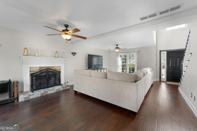 living area with baseboards, visible vents, dark wood finished floors, ceiling fan, and a stone fireplace