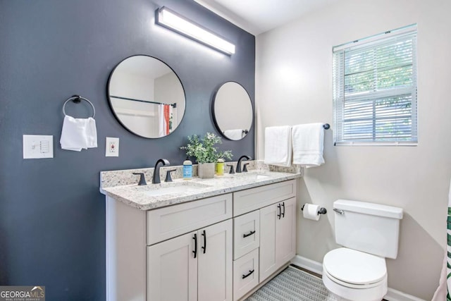 bathroom with toilet, double vanity, baseboards, and a sink