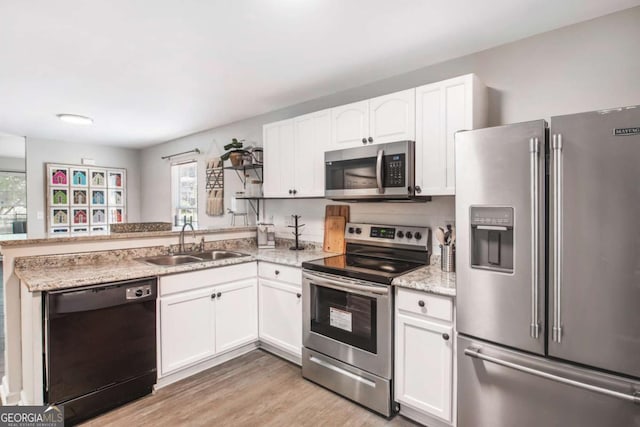 kitchen featuring light wood-style flooring, appliances with stainless steel finishes, white cabinetry, a sink, and a peninsula