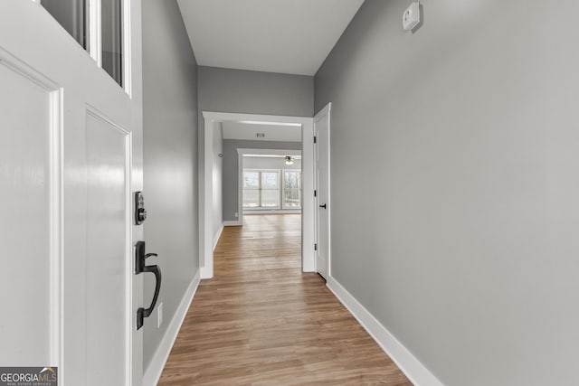 corridor featuring light wood-style flooring and baseboards