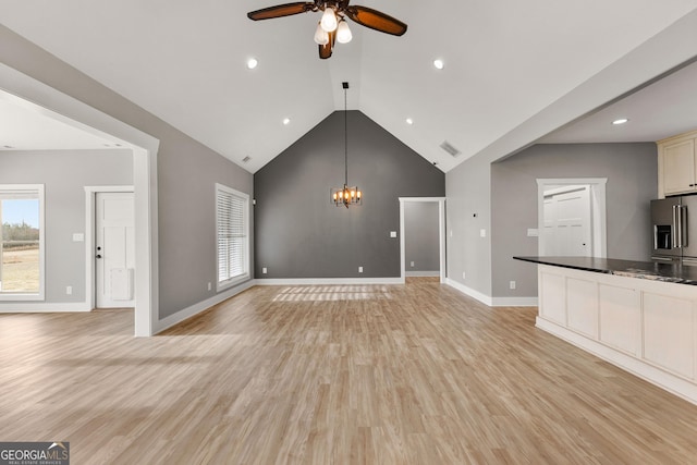 unfurnished living room featuring ceiling fan with notable chandelier, light wood-type flooring, plenty of natural light, and baseboards