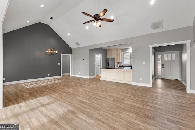 unfurnished living room with light wood-type flooring, high vaulted ceiling, visible vents, and ceiling fan with notable chandelier