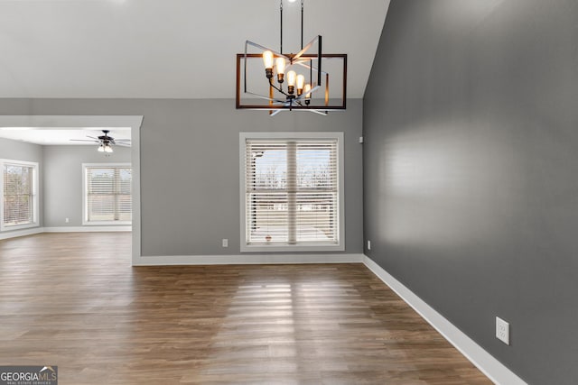 unfurnished dining area featuring ceiling fan with notable chandelier, wood finished floors, and baseboards