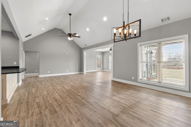 unfurnished living room featuring ceiling fan with notable chandelier, high vaulted ceiling, light wood-type flooring, and visible vents