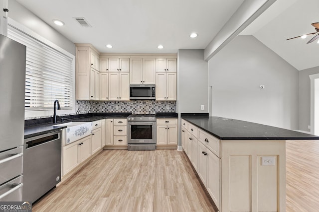 kitchen featuring appliances with stainless steel finishes, a sink, a peninsula, and cream cabinets