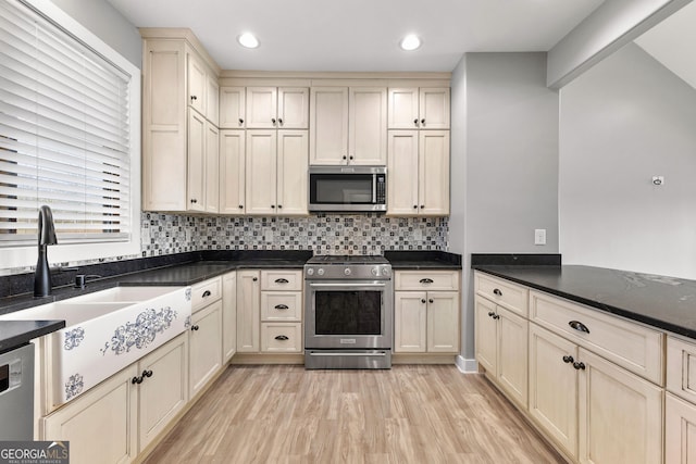 kitchen featuring appliances with stainless steel finishes, light wood-style floors, a sink, and dark countertops