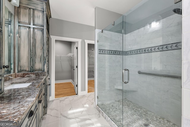 bathroom with a walk in closet, marble finish floor, a stall shower, vanity, and baseboards