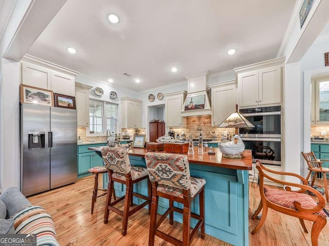 kitchen with light wood finished floors, stainless steel appliances, decorative backsplash, ornamental molding, and an island with sink