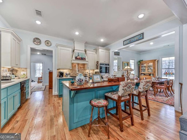 kitchen featuring blue cabinetry, visible vents, wooden counters, light wood-type flooring, and a kitchen breakfast bar