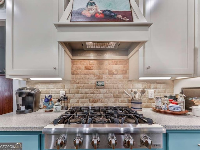 kitchen with light stone counters, white cabinetry, backsplash, range, and custom range hood